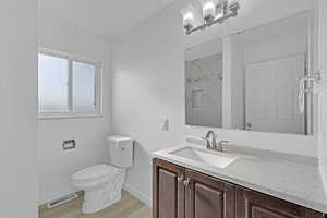 Bathroom featuring tiled shower, hardwood / wood-style floors, vanity, and toilet