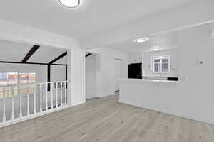 Unfurnished living room featuring sink, beamed ceiling, light hardwood / wood-style floors, and a textured ceiling