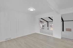 Spare room featuring beamed ceiling, light hardwood / wood-style floors, and wood walls