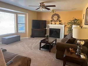 Living room with ceiling fan, a fireplace, carpet, and a textured ceiling