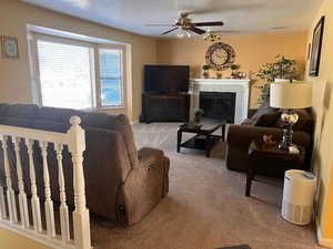 Carpeted living room with ceiling fan, a fireplace, and a textured ceiling