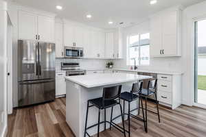 Kitchen featuring a center island, white cabinets, decorative backsplash, medium hardwood / wood-style floors, and stainless steel appliances