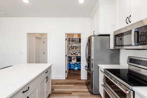 Kitchen with stainless steel appliances, medium hardwood / wood-style flooring, white cabinetry, and light stone counters