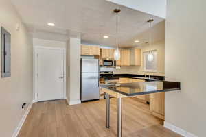 Kitchen featuring pendant lighting, light brown cabinets, light wood-type flooring, kitchen peninsula, and stainless steel appliances