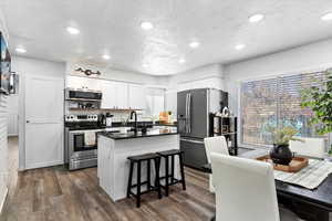 Kitchen featuring a kitchen bar, stainless steel appliances, dark wood-type flooring, a center island, and white cabinetry