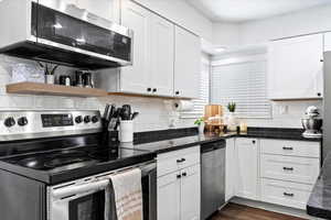 Kitchen featuring backsplash, dark stone counters, white cabinets, dark hardwood / wood-style floors, and stainless steel appliances