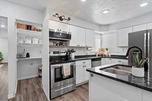 Kitchen featuring dark wood-type flooring, dark stone counters, white cabinets, sink, and stainless steel appliances