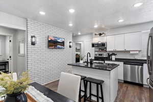 Kitchen with a kitchen island with sink, white cabinets, dark hardwood / wood-style floors, and appliances with stainless steel finishes