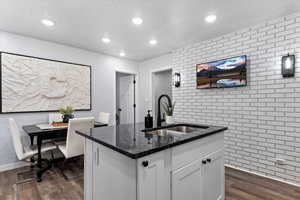 Kitchen featuring dark wood-type flooring, dark stone counters, sink, an island with sink, and white cabinetry