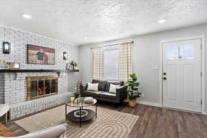 Living room featuring dark hardwood / wood-style flooring, a textured ceiling, and a brick fireplace