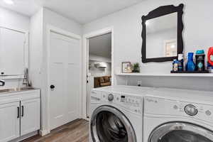 Clothes washing area with dark hardwood / wood-style floors, cabinets, independent washer and dryer, and sink