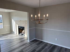 Unfurnished dining area with a chandelier, wood-type flooring, and a stone fireplace