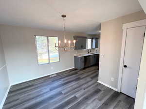 Kitchen featuring gray cabinetry, dark wood-type flooring, an inviting chandelier, sink, and stainless steel dishwasher