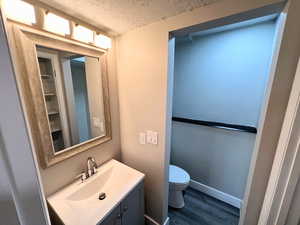 Bathroom with vanity, a textured ceiling, hardwood / wood-style flooring, and toilet