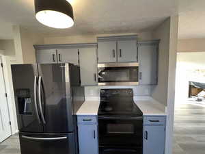 Kitchen featuring gray cabinets, light wood-type flooring, a textured ceiling, and appliances with stainless steel finishes