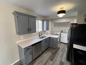 Kitchen with sink, stainless steel dishwasher, dark hardwood / wood-style floors, gray cabinets, and independent washer and dryer