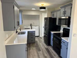 Kitchen featuring washer and clothes dryer, black appliances, sink, dark hardwood / wood-style floors, and gray cabinets