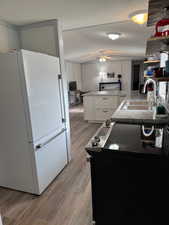 Kitchen featuring white cabinetry, black / electric stove, white fridge, light hardwood / wood-style floors, and a textured ceiling