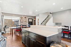 Kitchen with light stone countertops, dark hardwood / wood-style flooring, a center island, and stainless steel fridge