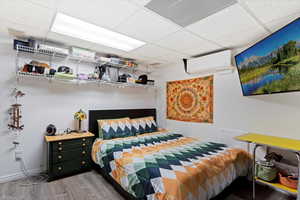 Bedroom with hardwood / wood-style flooring, a paneled ceiling, and a wall mounted air conditioner