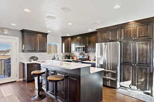 Kitchen with dark brown cabinets, a center island, stainless steel appliances, and dark hardwood / wood-style floors