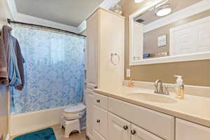 Full bathroom with a textured ceiling, toilet, shower / tub combo with curtain, vanity, and ornamental molding