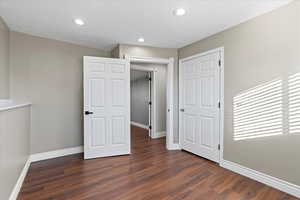 Unfurnished bedroom featuring a textured ceiling, a closet, and dark wood-type flooring