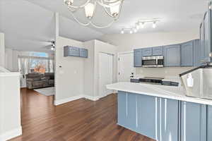 Kitchen with kitchen peninsula, ceiling fan with notable chandelier, stainless steel appliances, dark wood-type flooring, and lofted ceiling