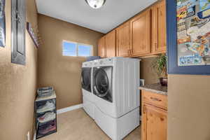 Laundry room featuring cabinets, light tile patterned floors, and washing machine and dryer