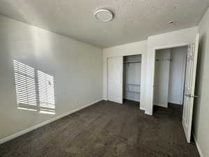 Unfurnished bedroom with dark colored carpet, a textured ceiling, and a closet