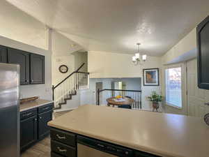 Kitchen featuring stainless steel appliances, vaulted ceiling, pendant lighting, an inviting chandelier, and light hardwood / wood-style floors