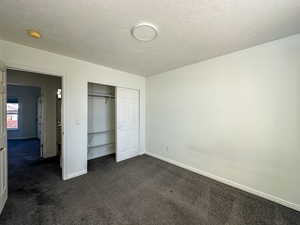 Unfurnished bedroom with dark carpet, a textured ceiling, and a closet