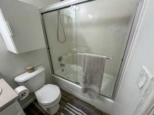 Full bathroom with shower / bath combination with glass door, wood-type flooring, vanity, and toilet