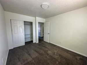 Unfurnished bedroom with dark carpet, a textured ceiling, and a closet