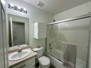 Full bathroom with combined bath / shower with glass door, vanity, a textured ceiling, and toilet