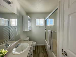 Full bathroom with vanity, toilet, enclosed tub / shower combo, a textured ceiling, and wood-type flooring