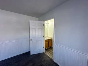 Unfurnished bedroom with wooden walls, sink, dark carpet, and lofted ceiling