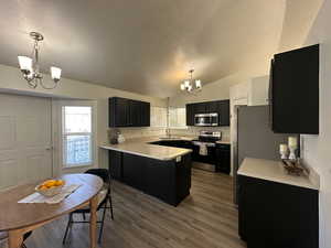 Kitchen with vaulted ceiling, hanging light fixtures, appliances with stainless steel finishes, and an inviting chandelier