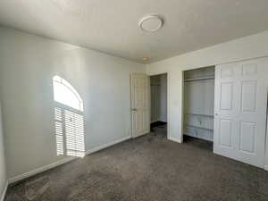 Unfurnished bedroom with dark colored carpet, a textured ceiling, and a closet