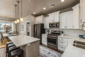 Kitchen with backsplash, an inviting chandelier, hanging light fixtures, appliances with stainless steel finishes, and white cabinetry