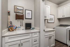 Clothes washing area featuring dark tile patterned flooring, cabinets, and washing machine and dryer