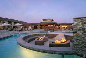 Pool at dusk featuring a patio, pool water feature, and an outdoor fire pit