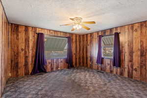 Spare room with carpet, a textured ceiling, ceiling fan, and wood walls