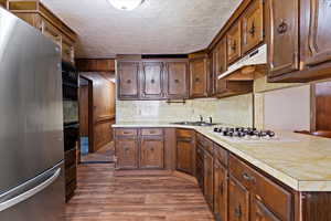 Kitchen with sink, white gas stovetop, dark hardwood / wood-style floors, stainless steel fridge, and black oven