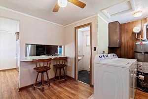 Laundry room with crown molding, ceiling fan, strapped water heater, independent washer and dryer, and wood-type flooring