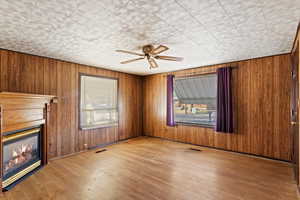 Unfurnished living room with hardwood / wood-style flooring, ceiling fan, and wooden walls