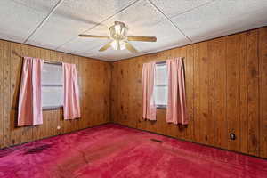 Carpeted spare room featuring a paneled ceiling, ceiling fan, and wooden walls