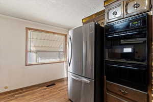 Kitchen with crown molding, black double oven, light wood-type flooring, a textured ceiling, and stainless steel refrigerator