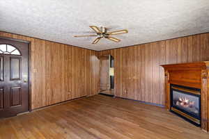 Unfurnished living room with hardwood / wood-style flooring, ceiling fan, and wood walls