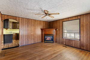 Unfurnished living room featuring wooden walls, sink, ceiling fan, and wood-type flooring